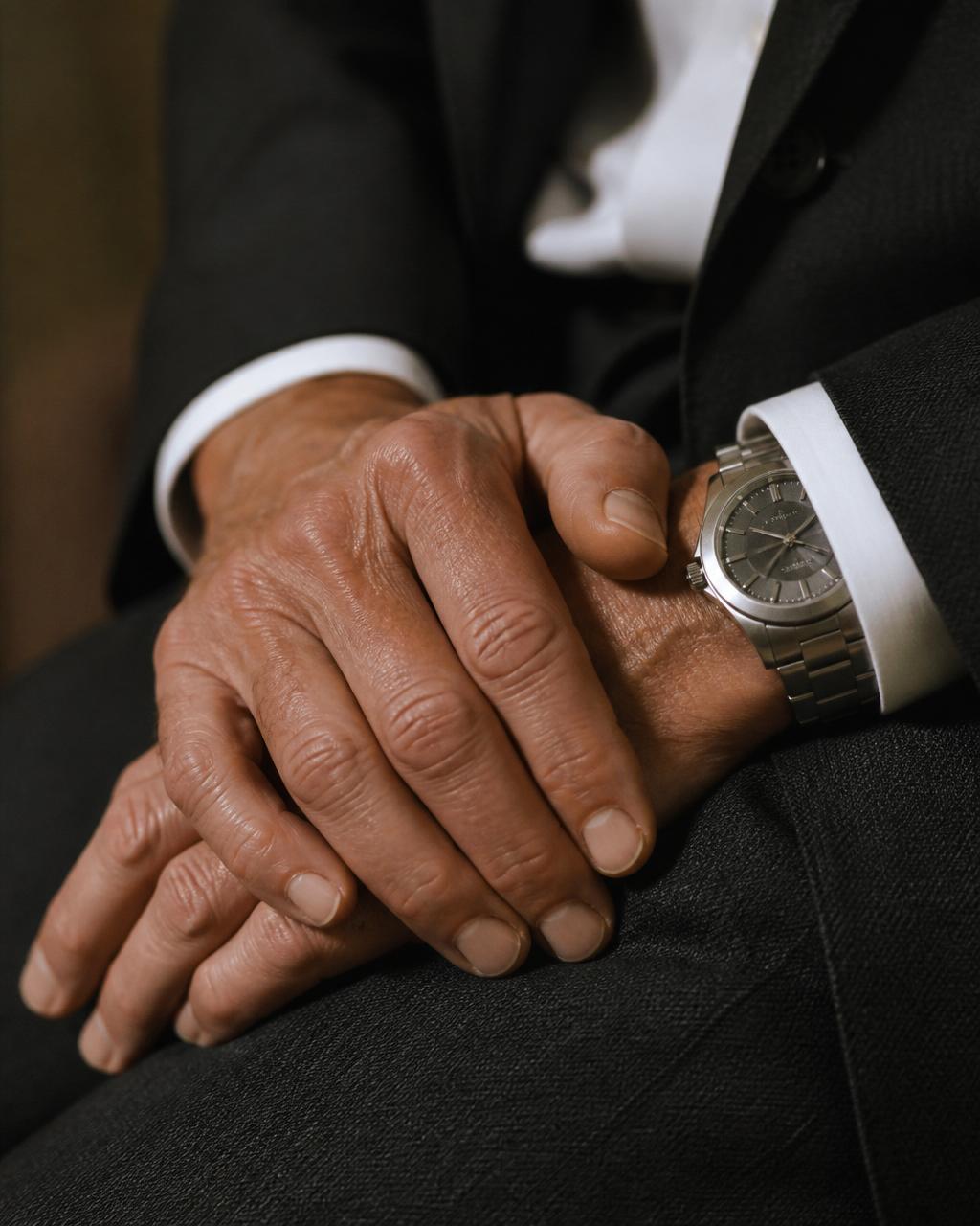 Editorial detail — hands and brushed steel wristwatch on charcoal suit